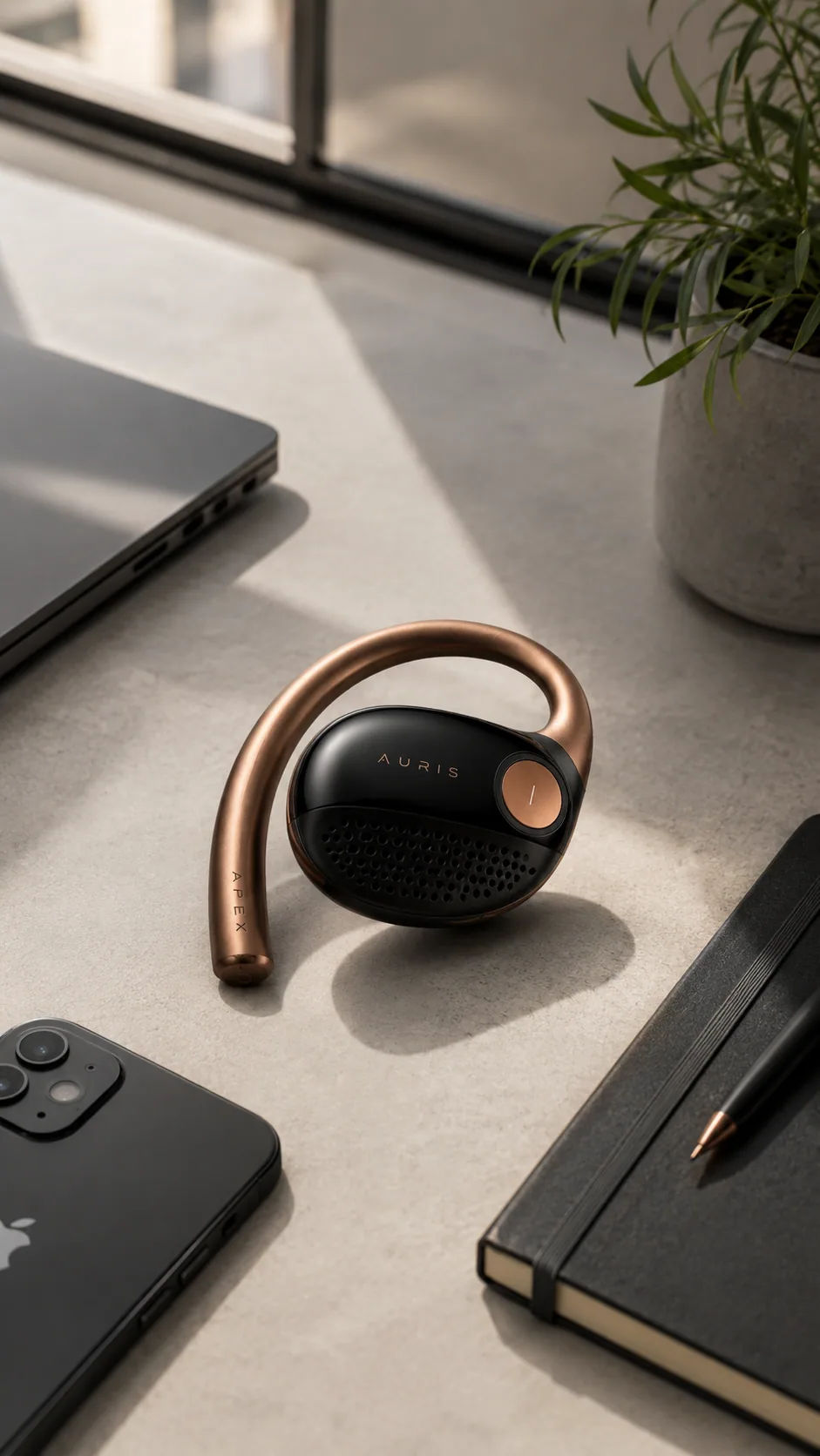 Auris wearable placed near a laptop, notebook, phone, and plant on a desk
