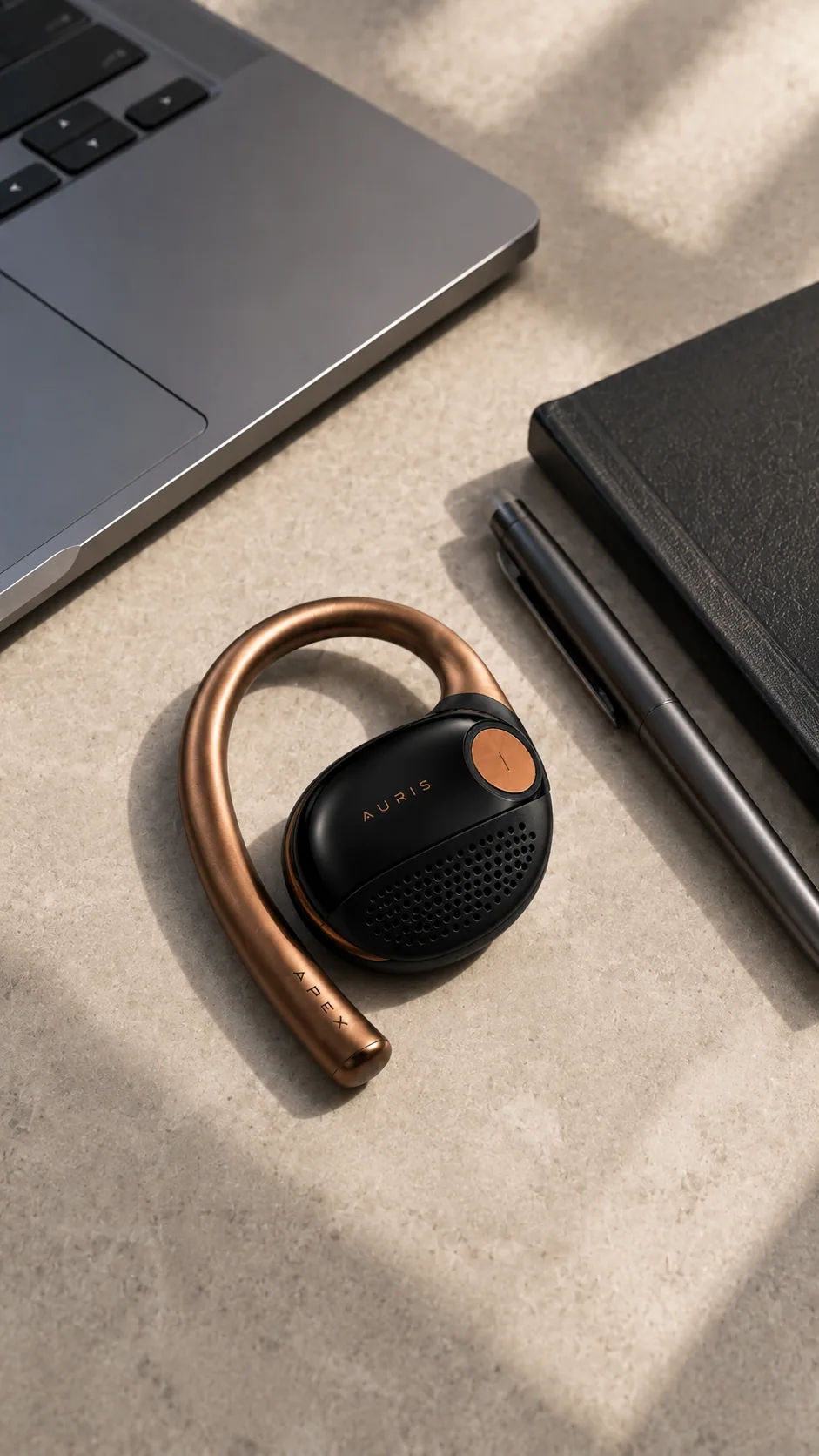 Auris wearable placed near a laptop and black notebook on a bright desk