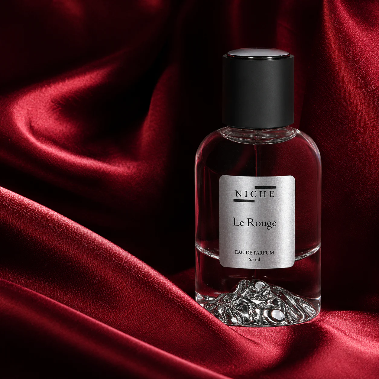 Le Rouge by Niche perfume bottle resting against deep red silk