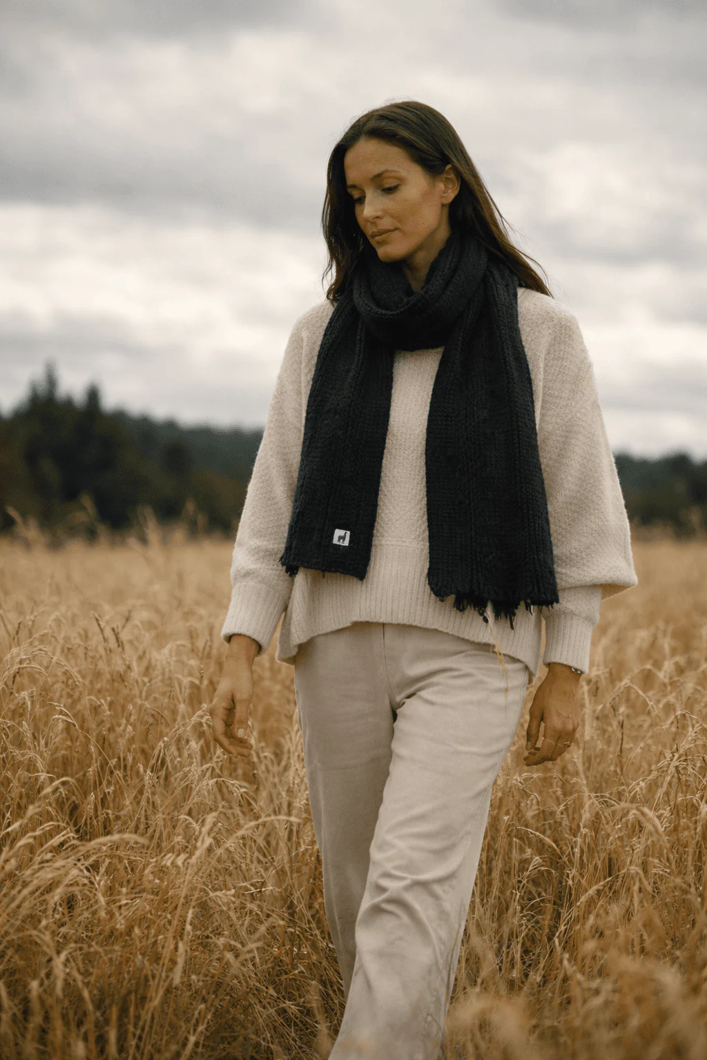 Woman wearing a black Pokoloko scarf while walking through a wheat field