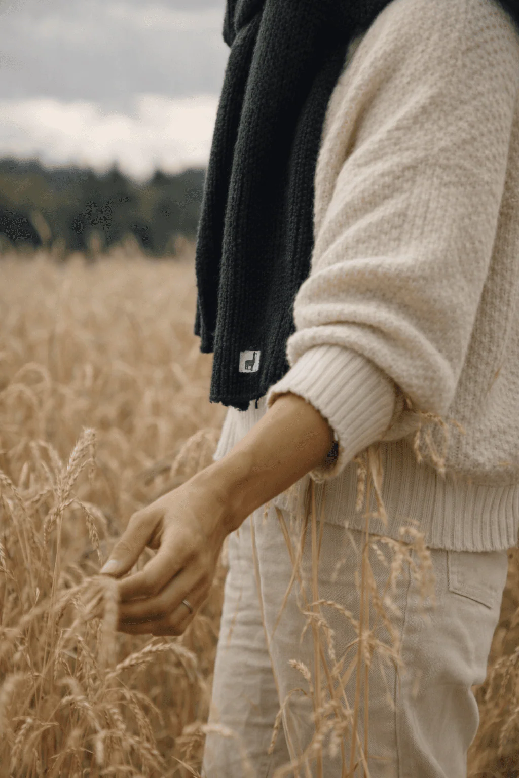 Close-up of the black Pokoloko scarf and neutral knitwear in a wheat field