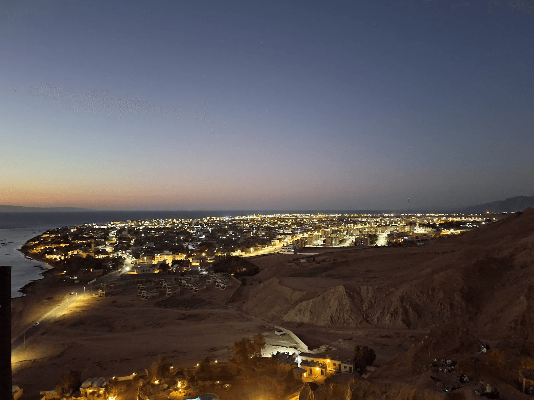 Coastal town lights viewed from the mountains after dusk
